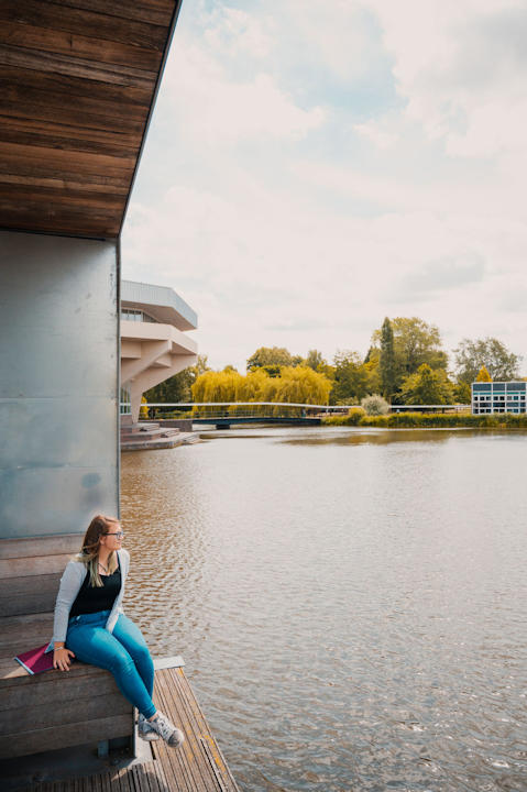 A student sits next to the lake, University of York campus